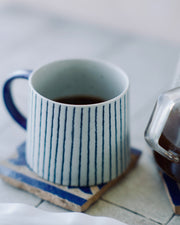 Mug with blue stripes filled with coffee on a wooden coaster.